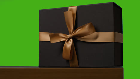 Close-Up-Of-Gift-Wrapped-Present-Decorated-With-Ribbon-On-Table-Shot-Against-Green-Screen-1